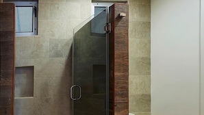 A bathroom with a glass shower enclosure, a toilet, and a small window.