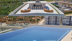 A rooftop pool with clear blue water, a view of the ocean, and a modern building with a circular design in the background.