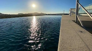 A waterfront view with a clear sky, a sun reflecting on the water, and a modern building with glass windows.