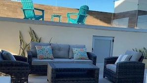 An outdoor seating area with wicker furniture and a sofa, a door, and a wall with a window.