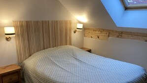 Ein Schlafzimmer mit geneigter Decke, einem Holzkopfende, einem Bett mit kariertem Überwurf, zwei Nachttischen und Wandleuchten zum Lesen.