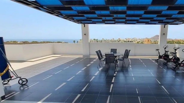 A covered outdoor area with a table and chairs, exercise bikes, and a scooter. - Condos TE22 (Cabo San Lucas)