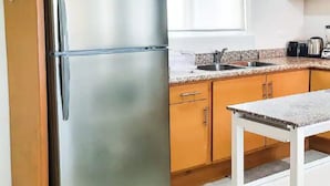 A kitchen with wooden cabinets, a stainless steel refrigerator, a granite countertop, and a white table. - Condos TE22 (Cabo San Lucas)