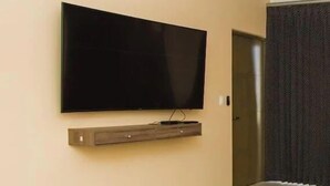 A modern living room with a flat-screen TV mounted on a wooden shelf, a ceiling fan, and a door leading to another room. - Condos TE22 (Cabo San Lucas)