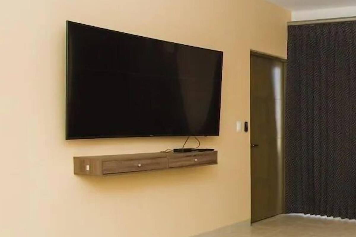 A modern living room with a flat-screen TV mounted on a wooden shelf, a ceiling fan, and a door leading to another room.