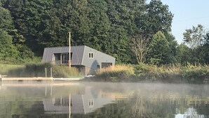 Una casa moderna junto a un lago tranquilo con un muelle, rodeada por un bosque denso.