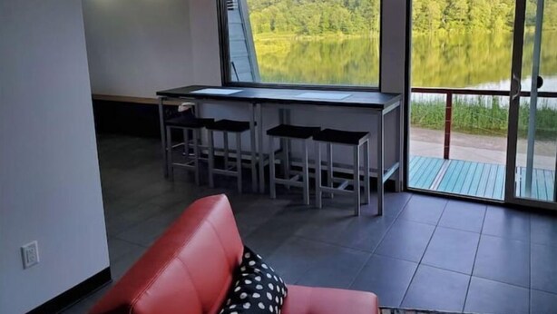 Una habitación moderna con un ventanal grande, un sofá rojo, una mesa de comedor con sillas y vistas a un área boscosa.