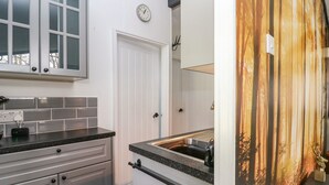 Et moderne køkken med en sort bordplade, hvide skabe og en rustfri stålvask samt et ur på væggen.