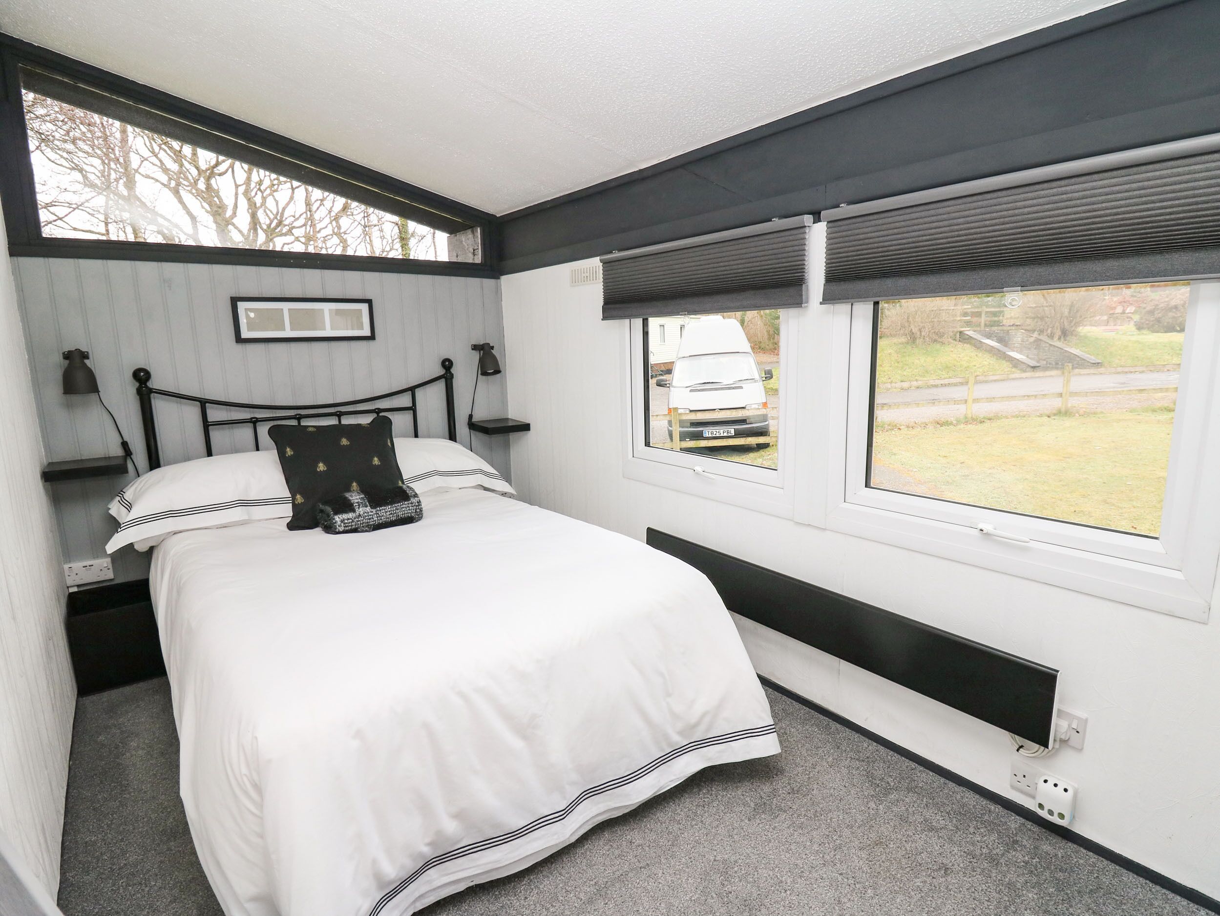 A bedroom with a bed, bedside lamps, a window with a view of the outside, and a radiator.