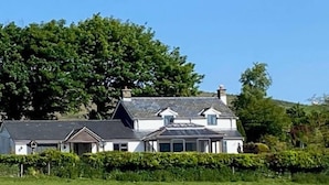 A two-story house with a sloped roof, surrounded by a well-maintained lawn and dense trees. - 3-bed Cottage Near Lake Vyrnwy, Garden & Petsok (Oswestry)
