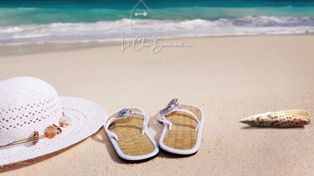Escena de playa con sombrero blanco, chanclas y una concha marina en la arena, con vista despejada al océano y un logo en el cielo.