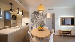Una cocina moderna con una isla central, sillas blancas, un frutero e iluminación colgante.