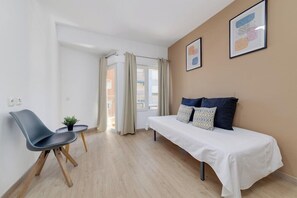 A modern room with a bed, a chair, a small table with a plant, and a window with curtains. - Madrid Hotel (Torrevieja)