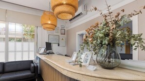 A reception area with a curved counter, a black leather sofa, and a large potted plant. - Madrid Hotel (Torrevieja)