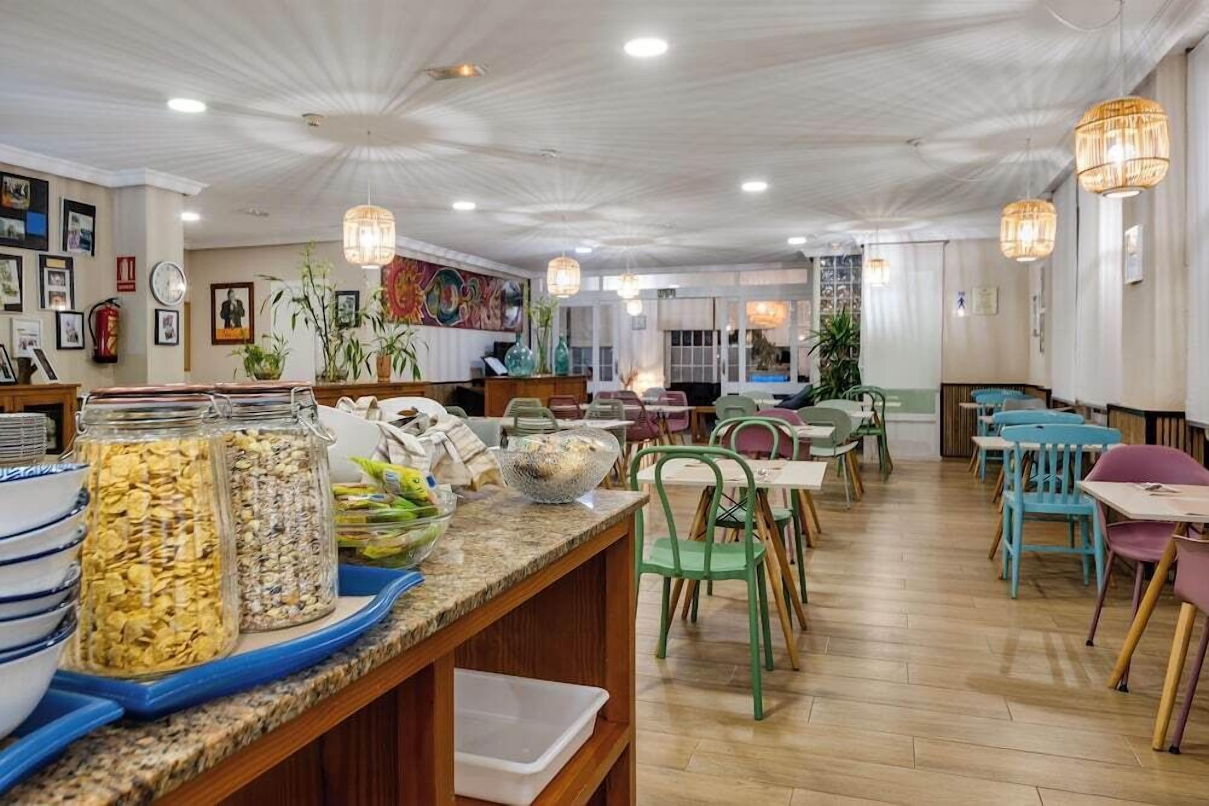 Un comedor con mesas y sillas de madera, una barra con productos alimenticios y luces colgantes.