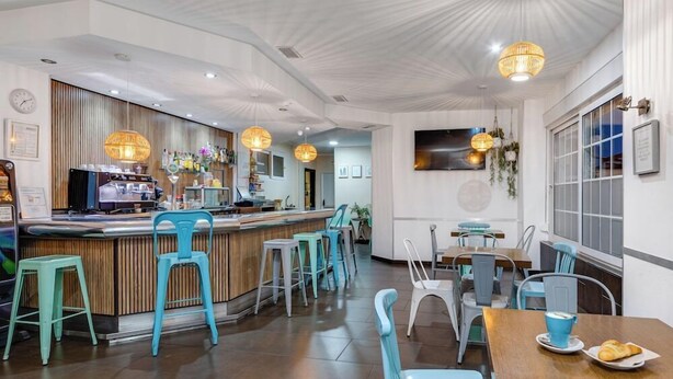 A modern cafe with a wooden counter, teal chairs, and pendant lighting. - Madrid Hotel (Torrevieja)
