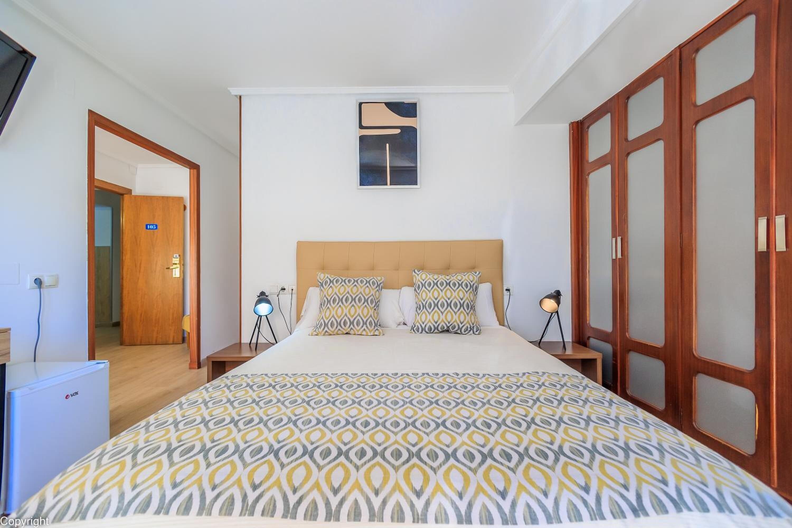 Een hotelkamer met een bed, bureau, stoel, lamp en kledingkast.