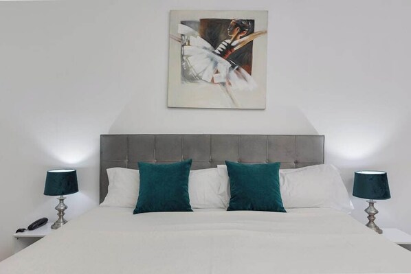 Une chambre avec un grand lit, deux tables de chevet avec des lampes et un tableau au mur.