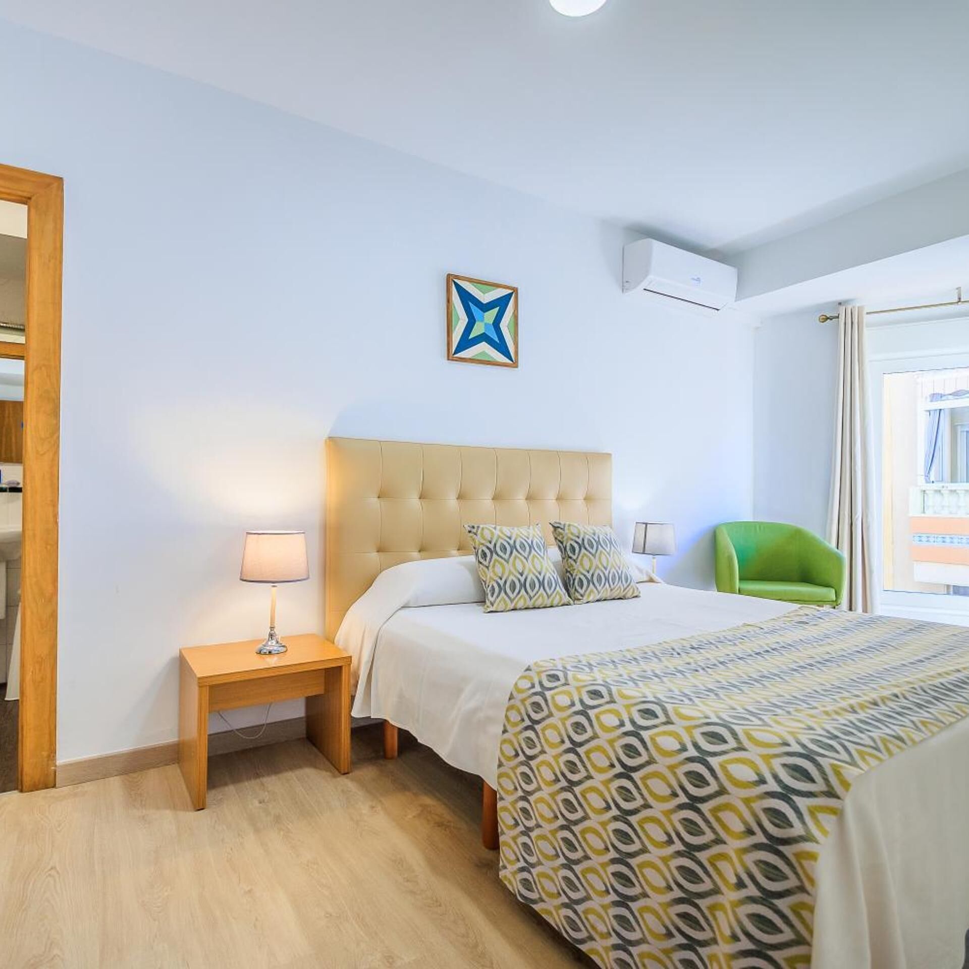 A hotel room with a bed, a nightstand, a green chair, a star decoration, and an air conditioning unit.