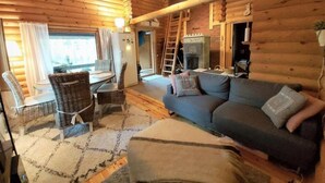 L’intérieur chaleureux d’un chalet, avec un revêtement mural en bois, un canapé, une table à manger avec des chaises et une cheminée.