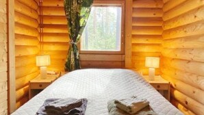 Une chambre aménagée dans un chalet en rondins, avec un lit, deux lampes de chevet et une fenêtre avec des rideaux.