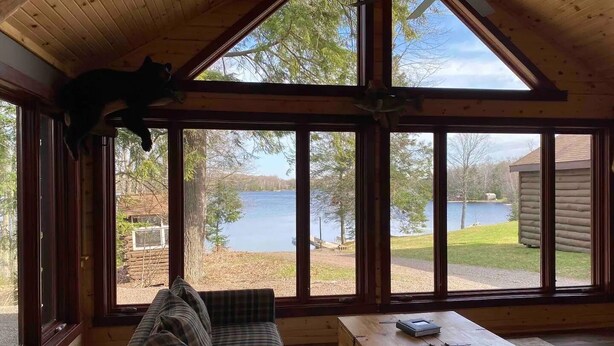 A cabin with a large window overlooking a lake, a plaid sofa, and a wooden chest. - Mercer, WI Beautiful Flambeau Flowage Cabin (Butternut)