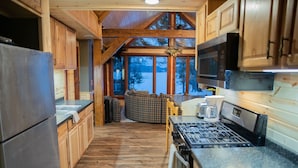 A wooden cabin kitchen with a stone countertop, a stove, and a view of a snowy landscape. - Mercer, WI Beautiful Flambeau Flowage Cabin (Butternut)