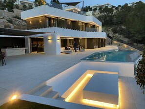 A modern two-story house with a swimming pool, outdoor seating, and a well-lit patio area. - Graham Holiday Rentals - Icon (Benissa)