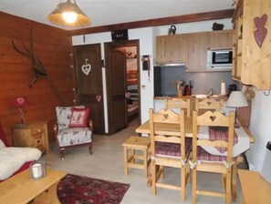 Cozy room with a wooden dining table, side table, and bed, plus a kitchen area with wooden cabinets.