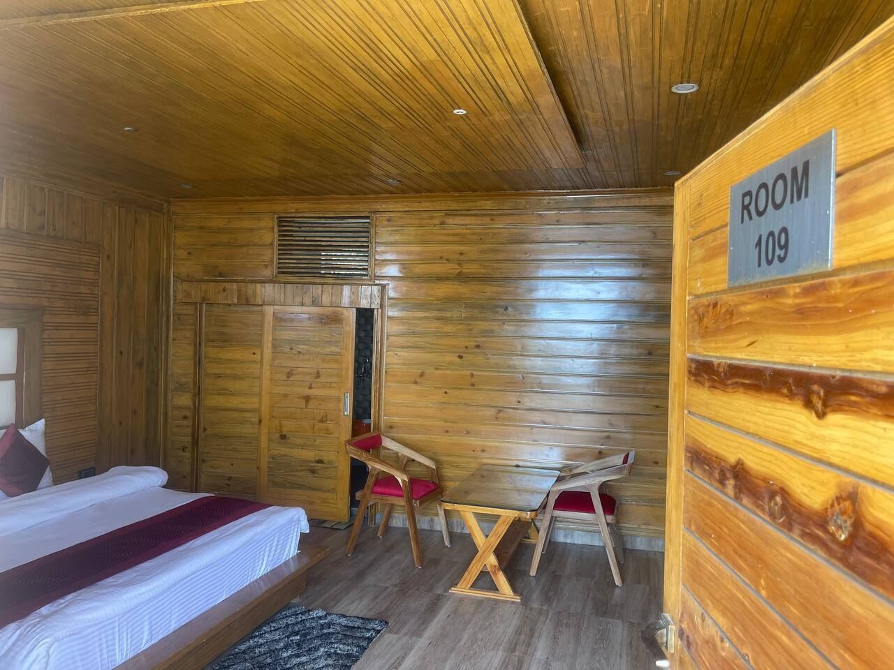 A wooden-paneled room with a bed, two chairs, a small table, and a sign indicating 'ROOM 109'.