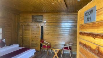 A wooden-paneled room with a bed, two chairs, a small table, and a sign indicating 'ROOM 109'.
