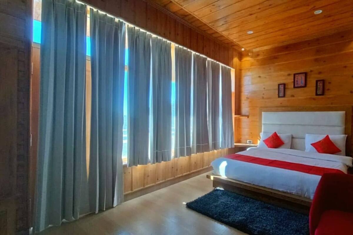 A wooden-paneled room with a bed, curtains, and a red chair.