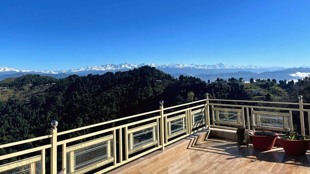 Un balcón con vistas a montañas nevadas y un valle boscoso.