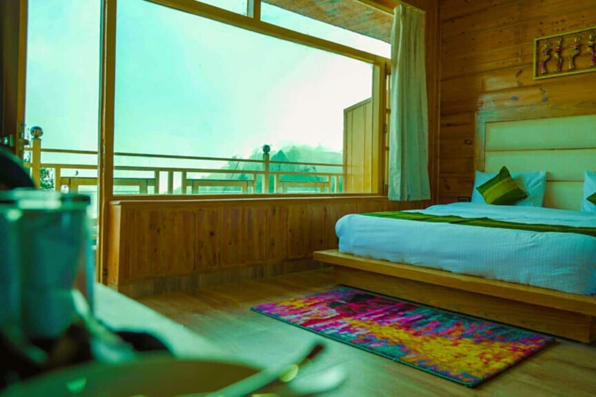 A wooden room with a bed, a colorful rug, and a window overlooking a balcony.