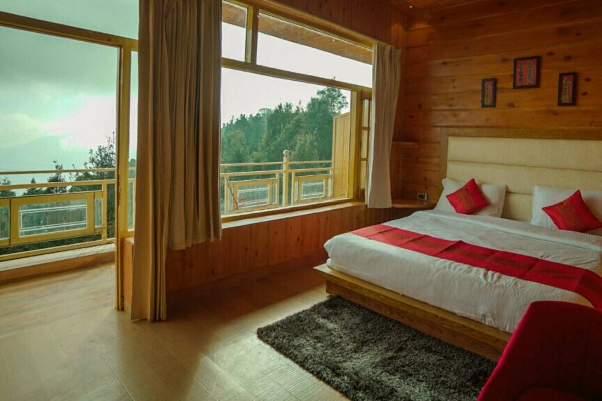 A wooden cabin bedroom with a large bed, a view of the outdoors, and a balcony.