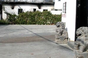 Un cortile con una statua di leone in pietra, un edificio bianco e un siepe.