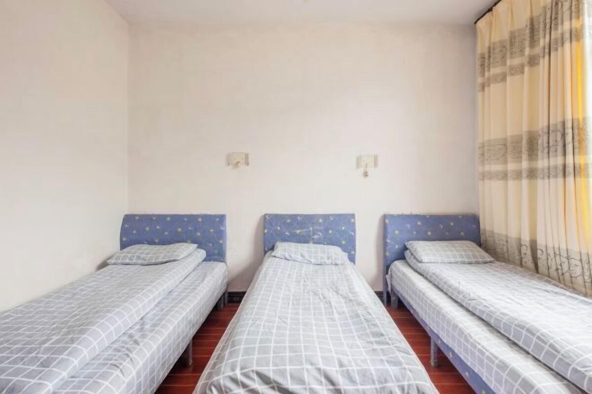 A room with three single beds, each with a blue headboard and a white bedspread.
