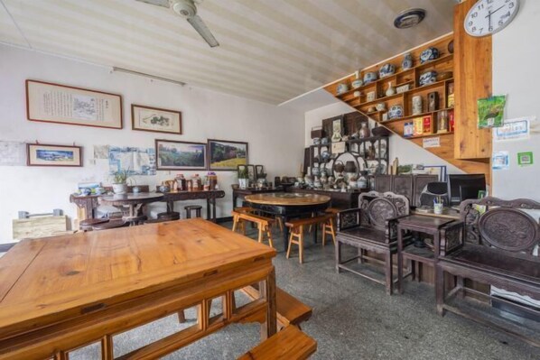 A room with a wooden dining table, multiple chairs, a staircase with shelves of decorative items, and framed pictures on the walls. - Qingyuan Farm Stay (Wuyuan)