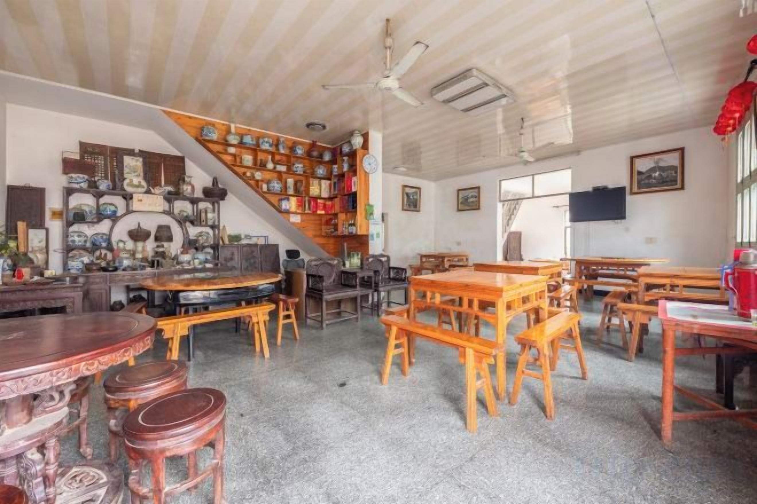 A room with a staircase, multiple tables, and chairs, and a variety of items on shelves.