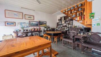 A room with a wooden dining table, chairs, a staircase with shelves, and various framed pictures on the walls.