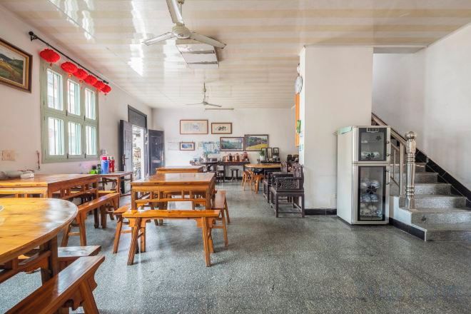 A spacious room with wooden tables and benches, a refrigerator, and a staircase.