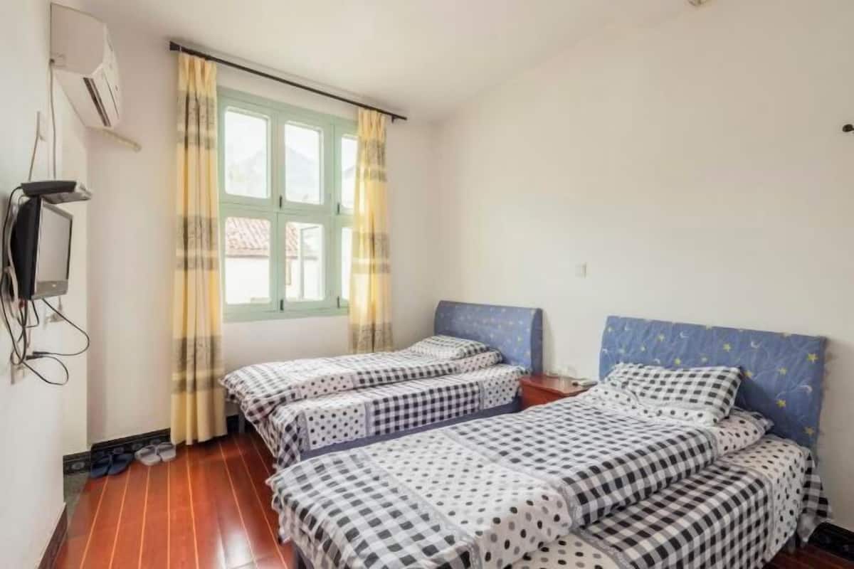 A room with two beds, a window with curtains, a television, and a wall-mounted air conditioner.