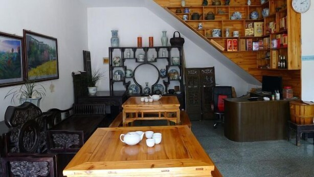A traditional room with a wooden table set for tea, a bookshelf with ceramics, and a painting on the wall. - Qingyuan Farm Stay (Wuyuan)