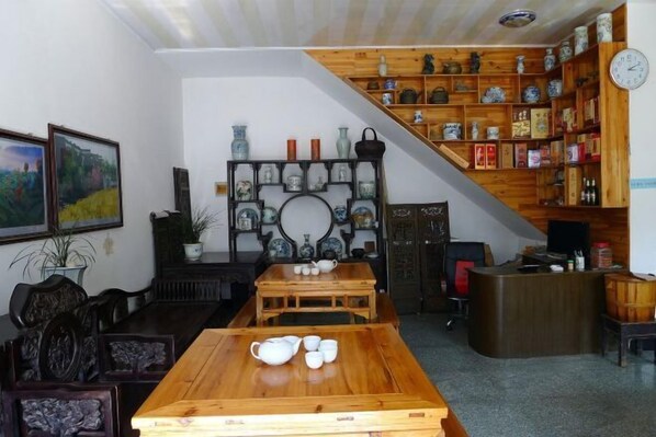A traditional room with a wooden table set for tea, a bookshelf with ceramics, and a painting on the wall.