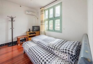 A small, tidy room with a bed, a television, a coat rack, and a window with curtains. - Qingyuan Farm Stay (Wuyuan)