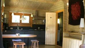 A cozy cabin interior with a wooden dining area, a kitchen with a stove, and a large window. - Chalet Kwikstaart on small-scale nature campsite 't Ol Gat (Zoutkamp)