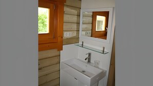 A bathroom with wooden walls, a white sink, a glass shelf, and a mirror. - Chalet Kwikstaart on small-scale nature campsite 't Ol Gat (Zoutkamp)