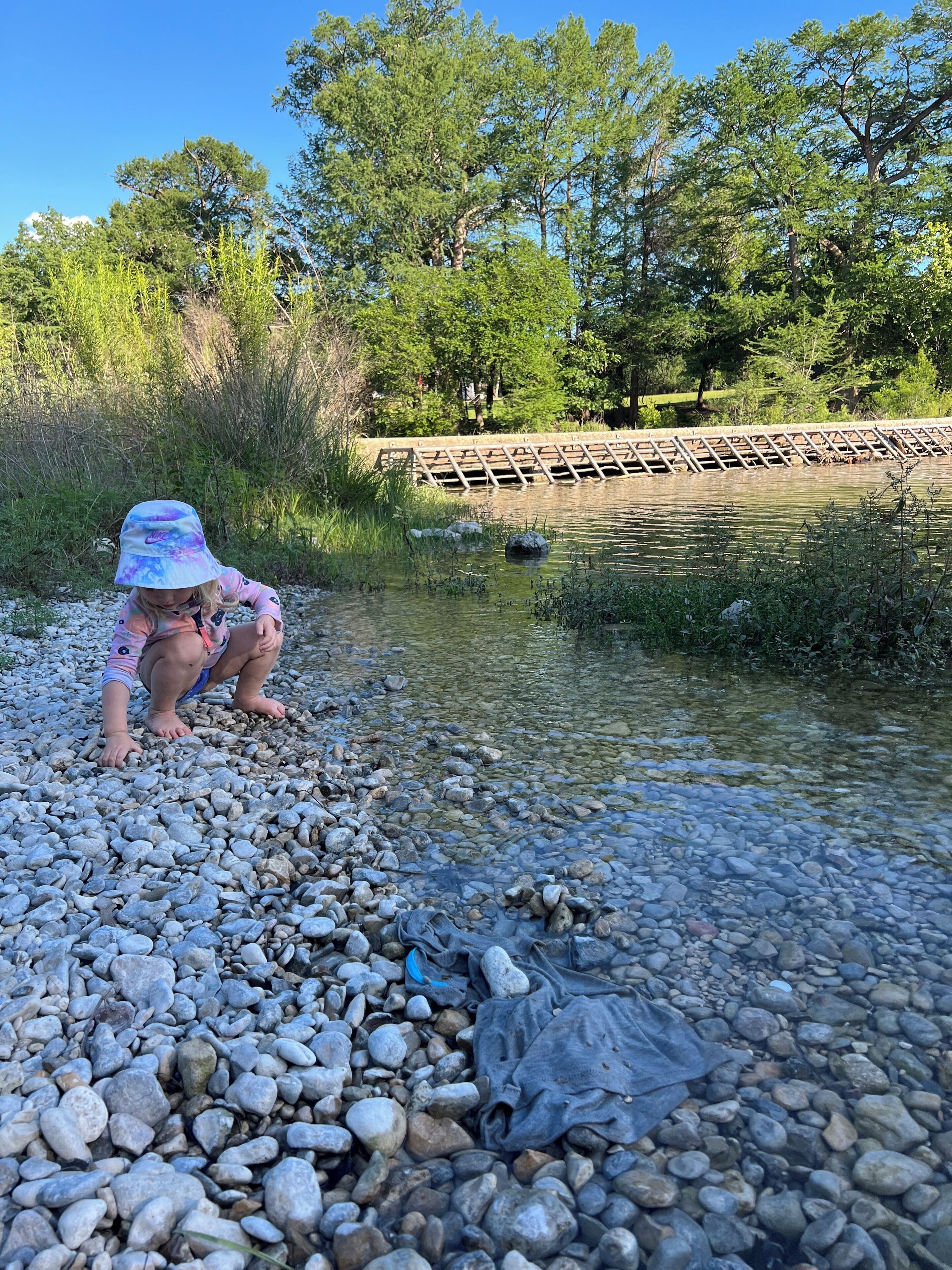 A child playing near a clear stream with pebbles and rocks.