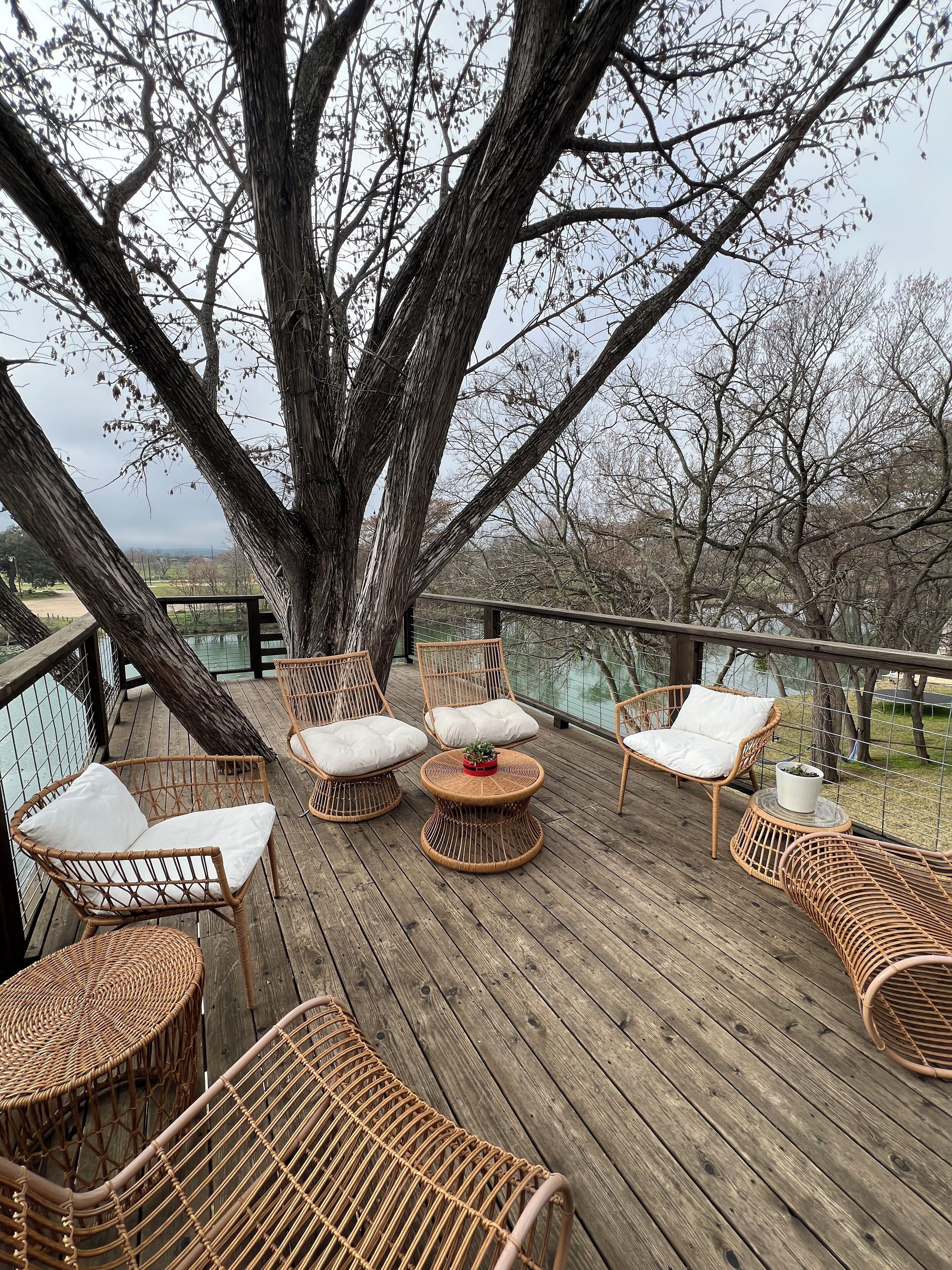 A wooden deck with wicker furniture and a view of trees and a distant landscape.