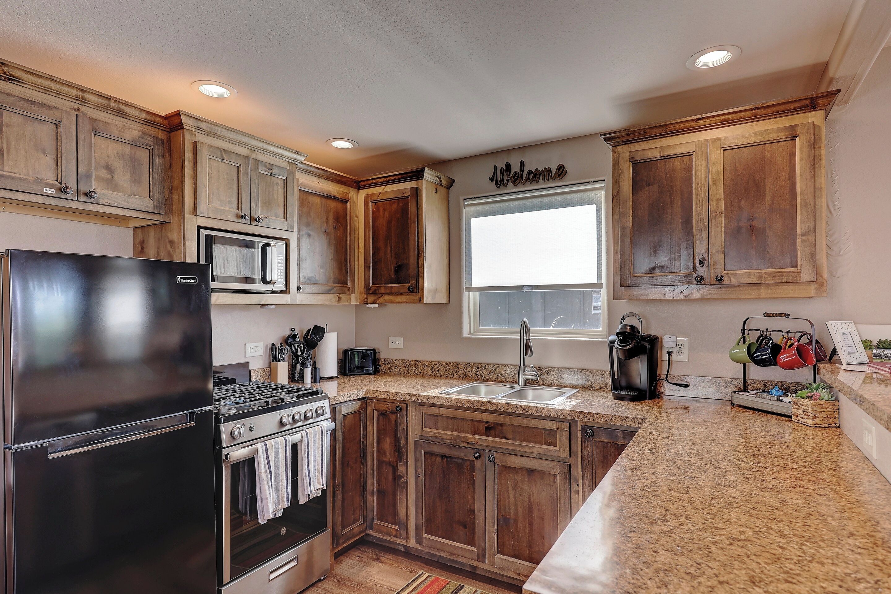 A kitchen with wooden cabinets, a stainless steel refrigerator, a microwave, a stove, and a window.
